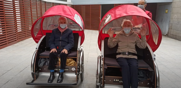 Residentes en silla de ruedas, con capotas de estilo turístico, acompañados por sus cuidadores mientras pasean por la ciudad