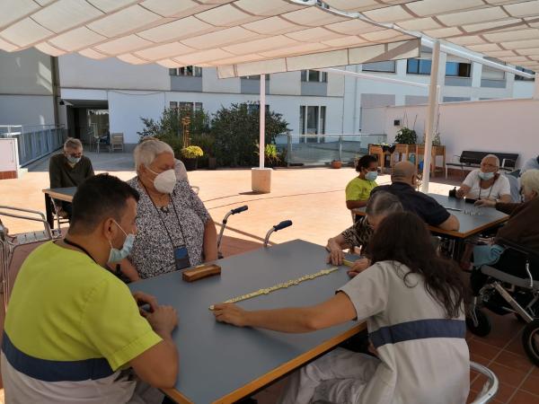 Residentes sentados en mesas, con cuatro personas por mesa, jugando al dominó