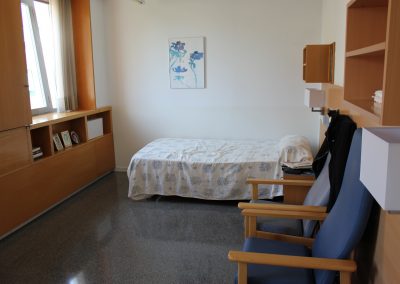 Una habitación de la residencia Fort Pienc, equipada con una cama, armarios y una estantería, que transmite una sensación de calma y serenidad