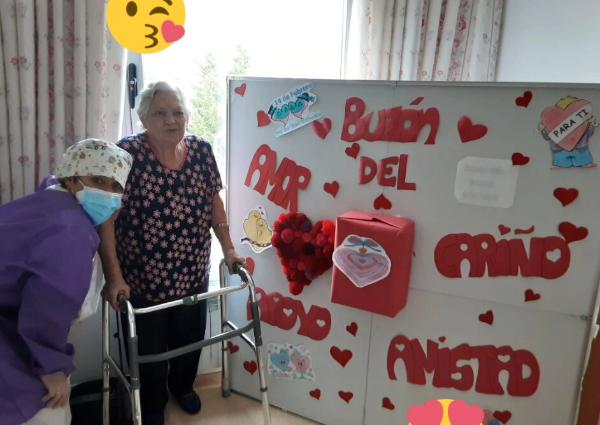 Una residente junto a una pizarra blanca grande colocada en el suelo, decorada con papel rojo cortado en forma de corazones y las palabras 'Amor' y 'Amistad' escritas