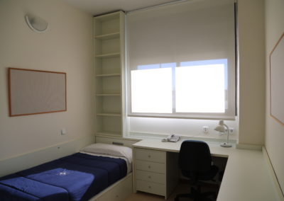 Habitación del Colegio Mayor UFV equipada con una cama, escritorio con cuatro cajones, lámpara