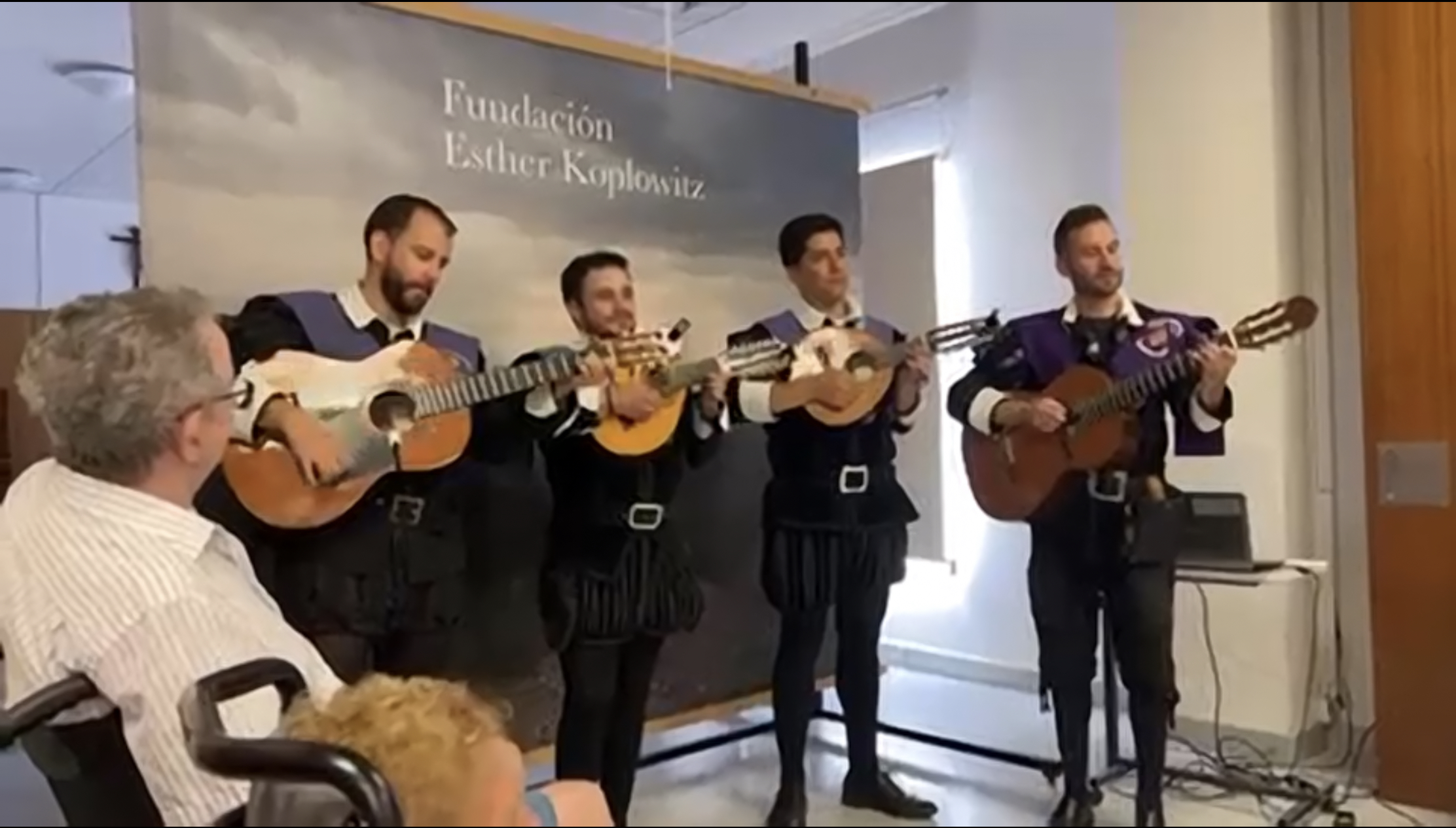 Cuatro hombres jóvenes de la Tuna de la UCM tocando la guitarra y realizando una actuación para los residentes de la residencia