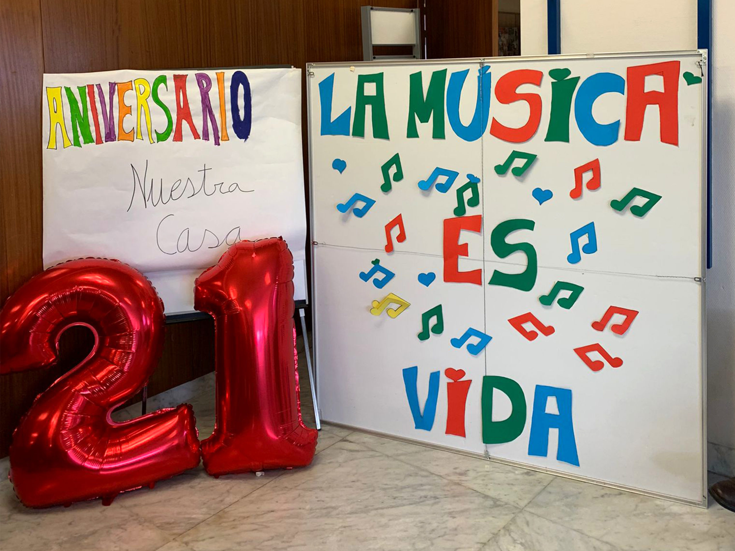 Carteles y globos decorativos con el texto "Aniversario Nuestra Casa 21 - La música es vida" en la celebración del XXI Aniversario de la residencia