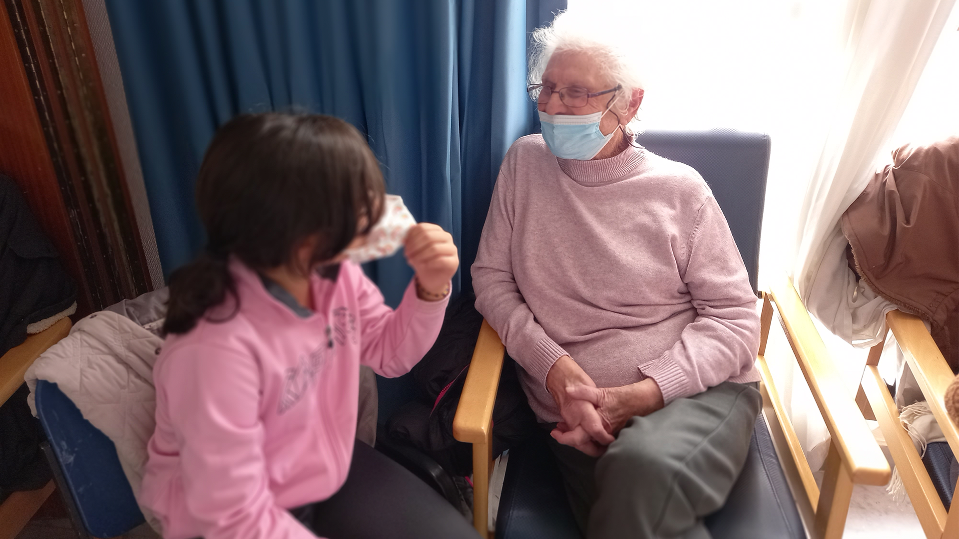 Una alumna del CEIPSO Príncipes de Asturias sentada en la residencia Nuestra Casa Collado Villalba, conversando con una residente mayor