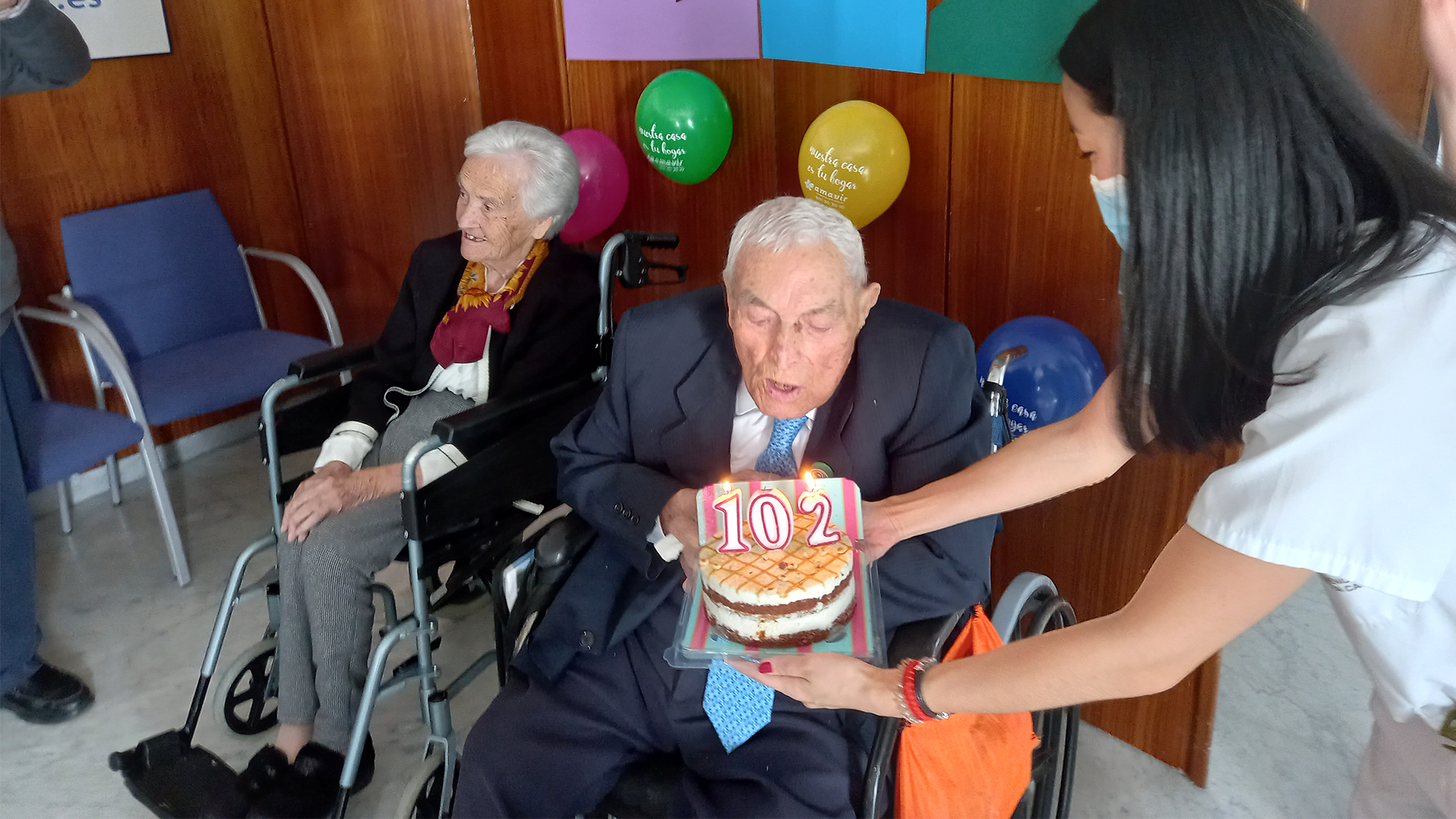 Don Casimiro Bachiller celebrando su 102 cumpleaños, soplando las velas de una tarta decorada con el número 102 frente a él