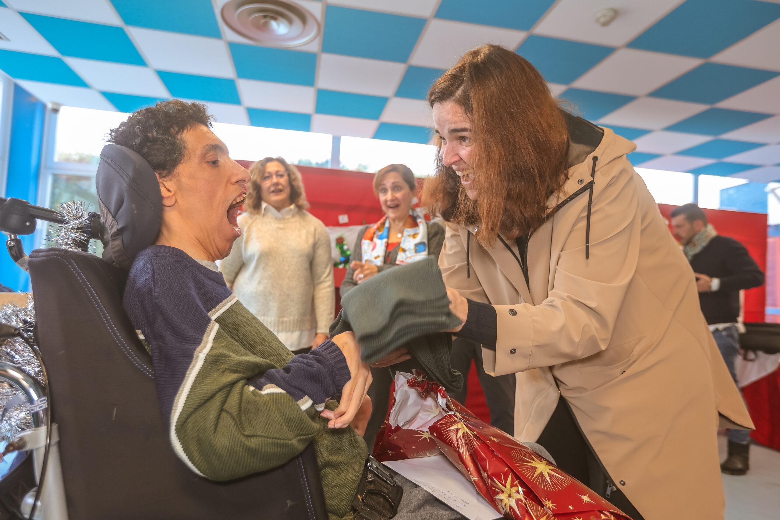 Un chico enfermo en silla de ruedas, con la boca abierta en señal de sorpresa, al recibir un regalo de los Reyes Magos